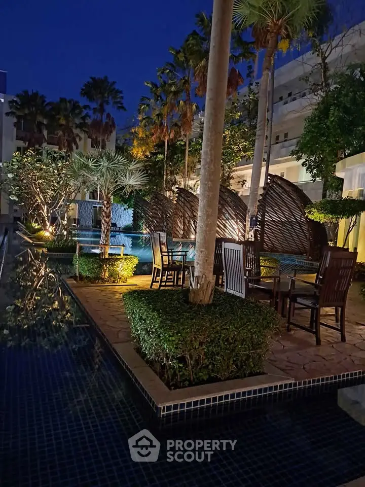 Luxurious outdoor pool area with elegant seating and lush greenery at night, perfect for relaxation and entertainment.