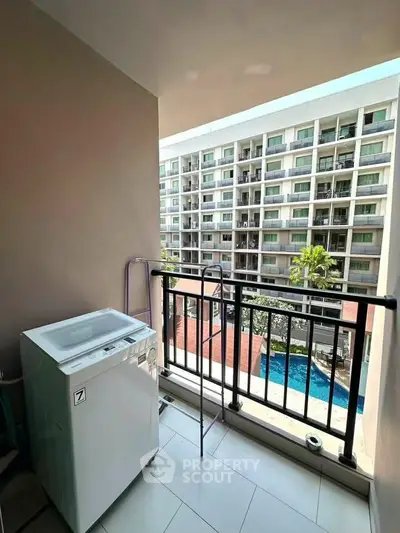 Modern balcony with washing machine overlooking pool and apartment complex.