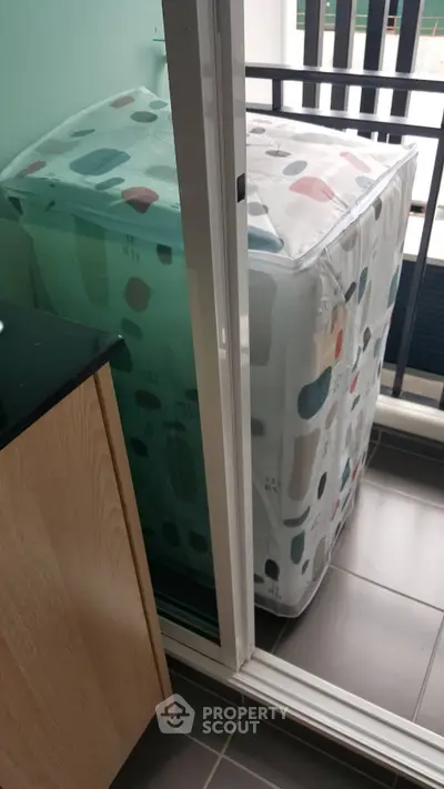Compact balcony with washing machine and sliding glass door in modern apartment.
