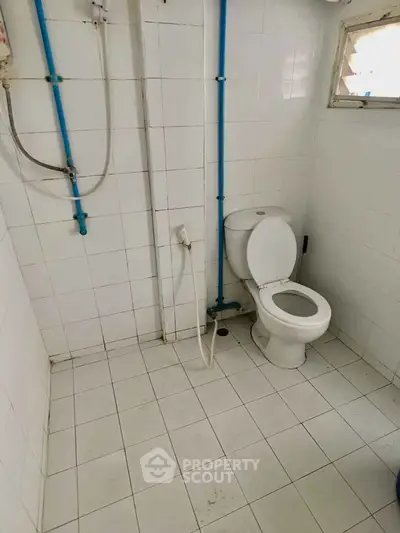 Simple white-tiled bathroom with toilet and shower in a compact layout.