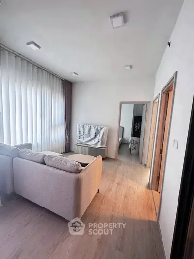 Modern living room with stylish sofa and natural light, leading to a cozy bedroom.