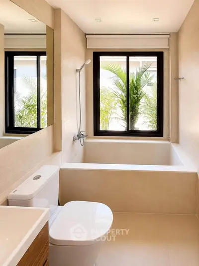 Modern bathroom with large window and bathtub offering serene garden view.