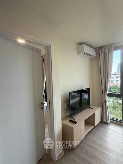 Modern living room with large window and city view, featuring a sleek TV setup and air conditioning.