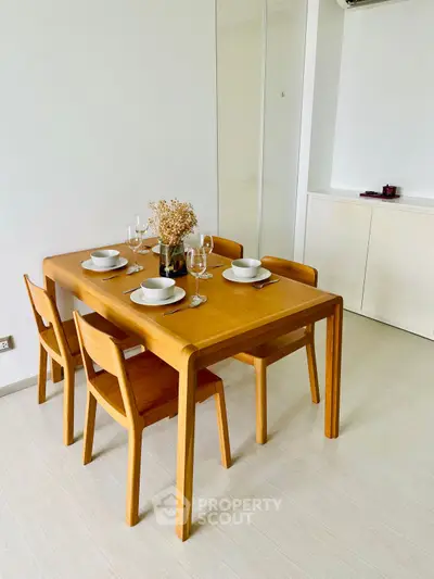 Modern dining area with wooden table and chairs, set for a meal in a minimalist interior.