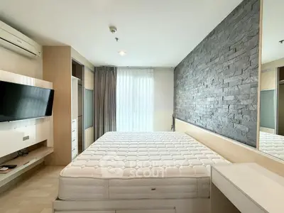 Modern bedroom with stone accent wall and mounted TV, featuring a spacious bed and ample natural light.