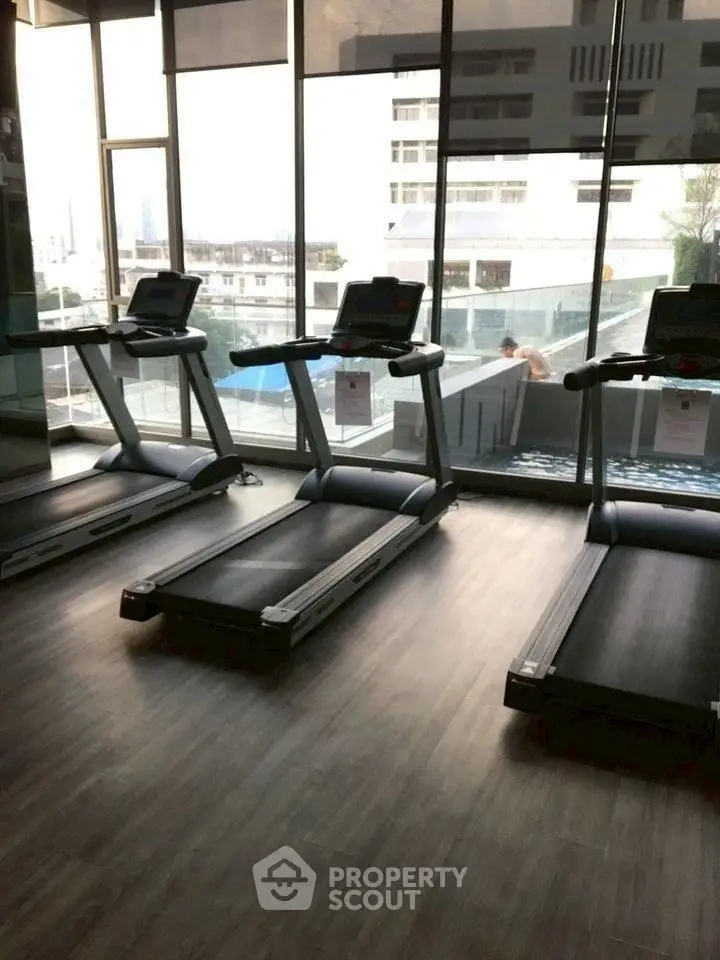 Modern gym with treadmills overlooking a pool and cityscape view.