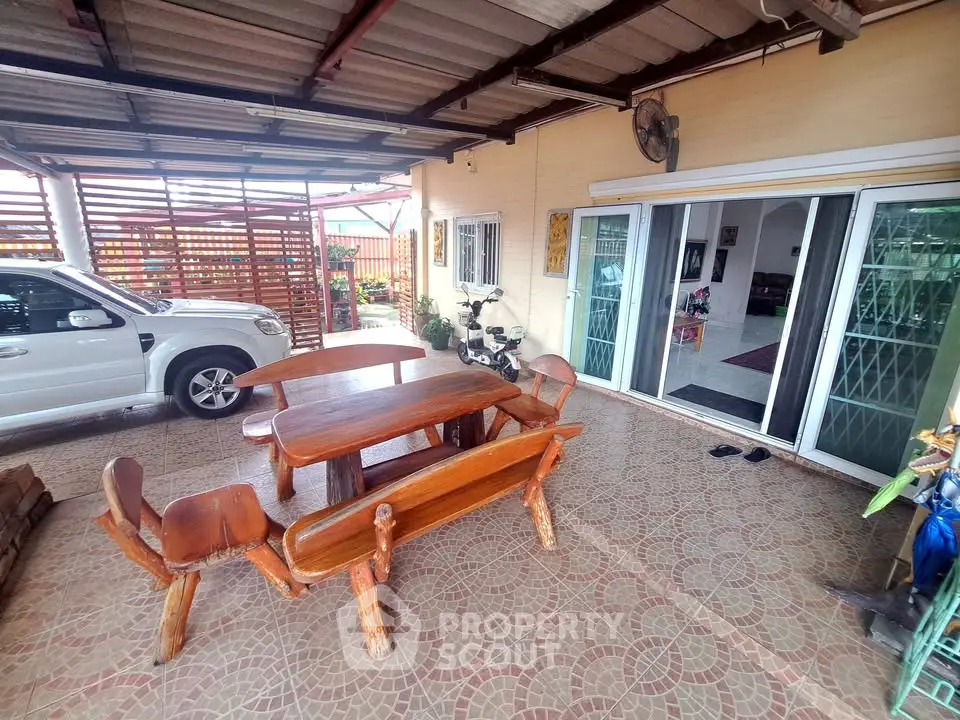 Charming covered patio with wooden furniture and adjacent carport in a cozy home setting.