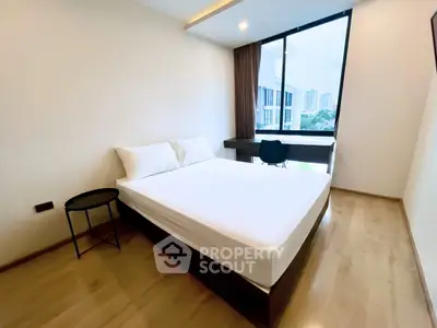 Modern bedroom with large window and city view, featuring a sleek desk and comfortable bed.