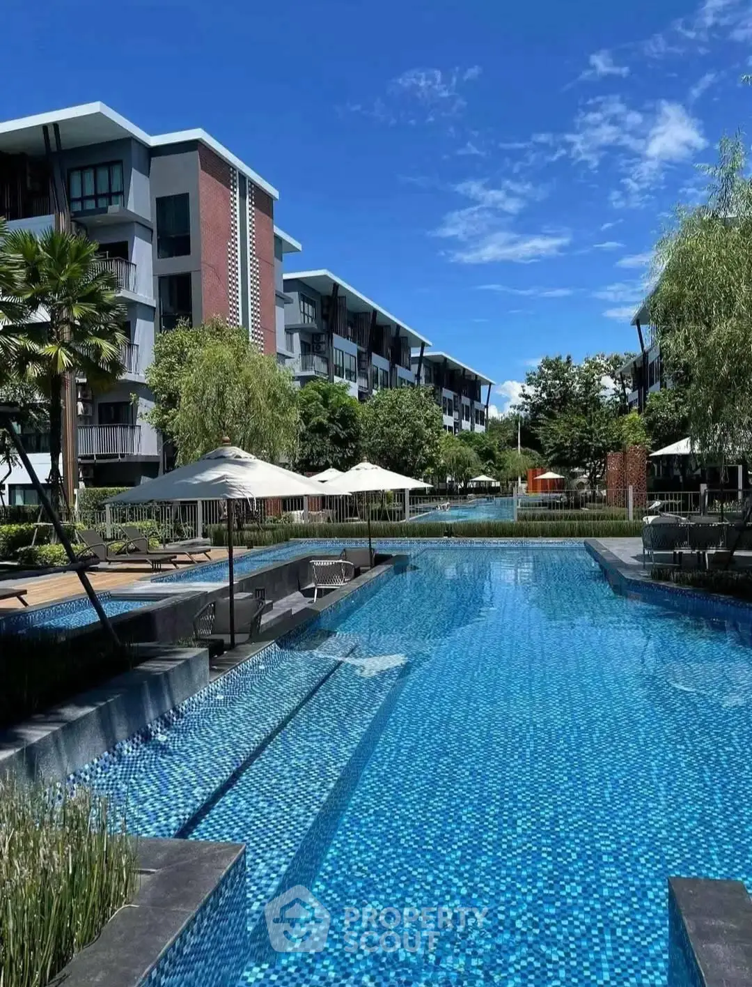 Luxurious residential complex with stunning pool and modern architecture under clear blue sky.