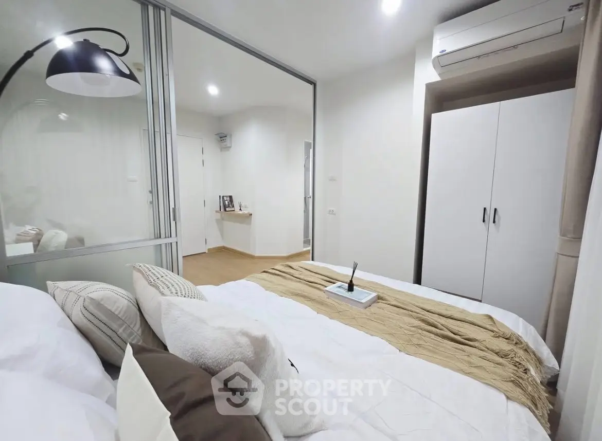Modern bedroom with cozy bedding and air conditioning unit, featuring a sleek white wardrobe.