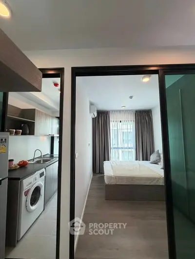 Modern apartment interior with kitchen and bedroom, featuring sleek design and natural light.