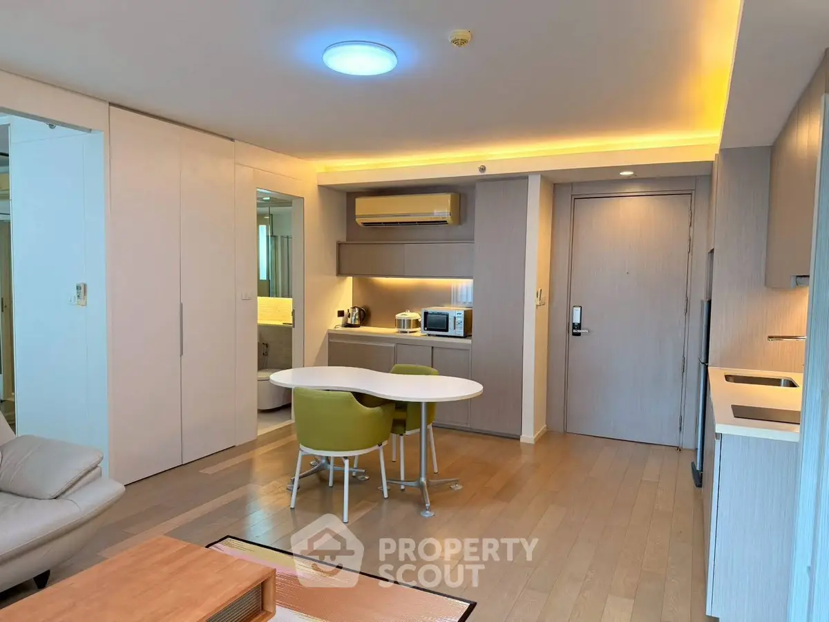 Modern open-plan living room with dining area and kitchenette, featuring sleek design and warm lighting.