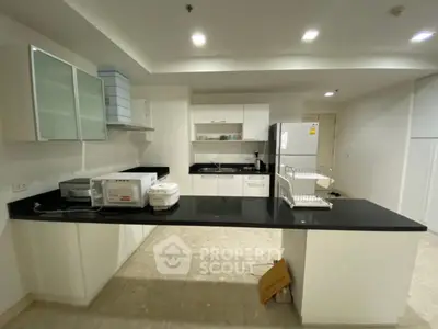 Modern kitchen with sleek black countertops and white cabinetry, featuring appliances like microwave and fridge.