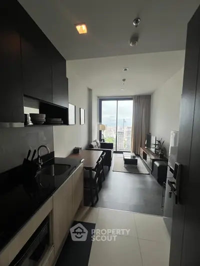Modern open-plan living room with kitchen and city view, featuring sleek furniture and large windows.