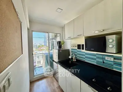 Modern kitchen with sleek black countertop and blue tile backsplash, featuring a microwave and fridge.