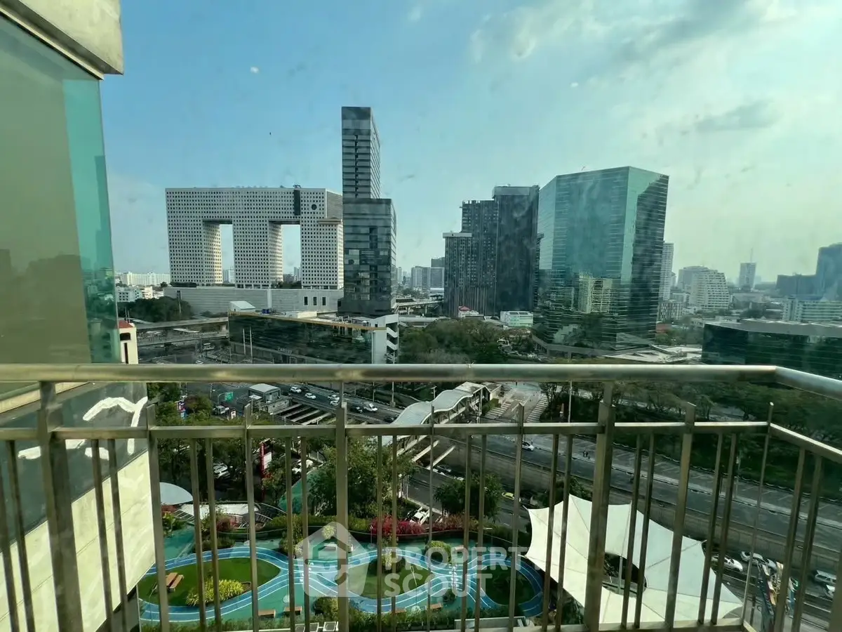 Stunning cityscape view from a high-rise balcony overlooking modern architecture and lush green spaces.