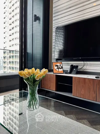 Modern living room with sleek TV setup and elegant glass coffee table with yellow tulips.