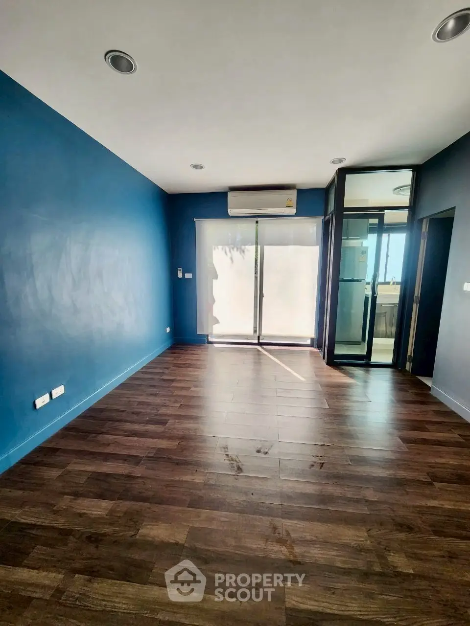 Spacious modern room with wooden flooring and large window for natural light.
