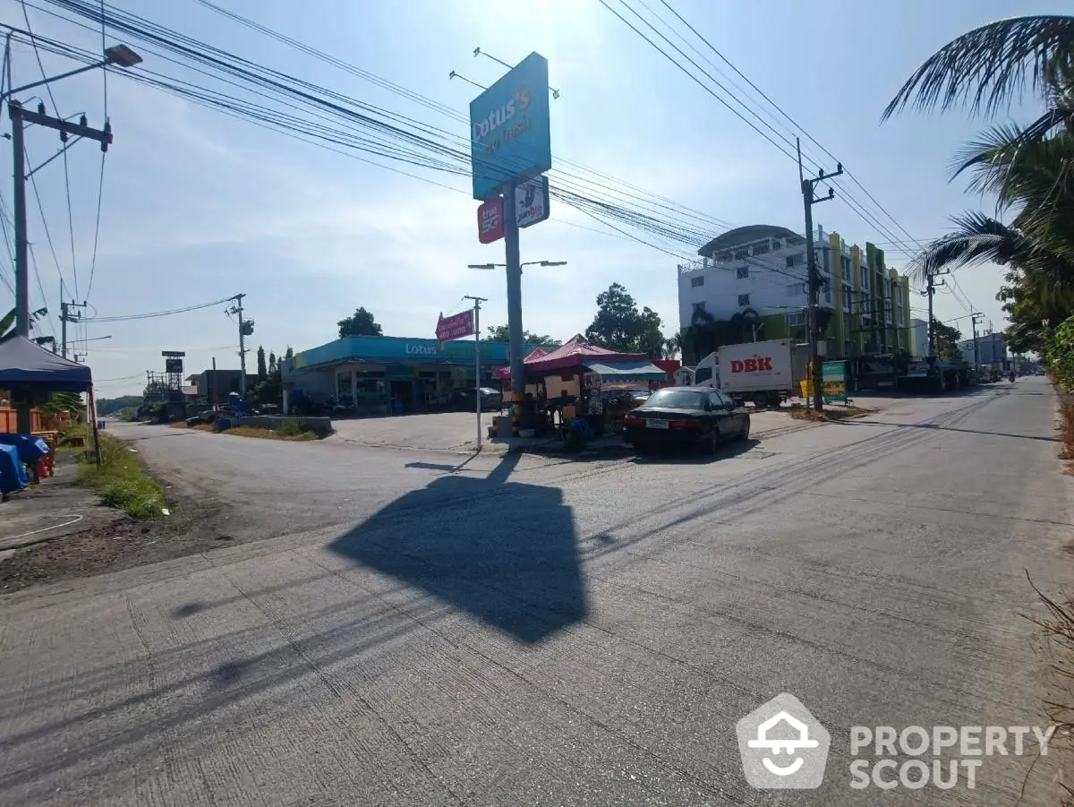 Street view of commercial area with shops and parked cars under clear blue sky.