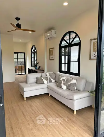 Stylish living room with modern L-shaped sofa and wooden flooring, featuring arched windows and cozy decor.
