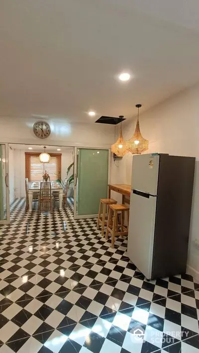 Stylish kitchen with modern fridge and elegant dining area, featuring chic lighting and checkered flooring.