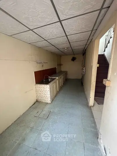 Spacious kitchen with vintage tile flooring and ceiling, featuring a long countertop and sink.
