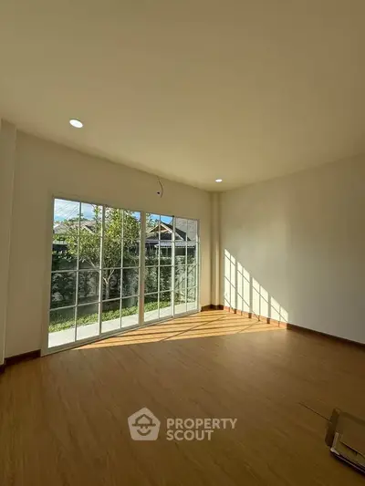 Spacious sunlit room with large windows and wooden flooring, perfect for a cozy living space.