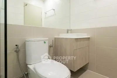 Modern bathroom with sleek fixtures and neutral tiles, featuring a compact vanity and toilet.