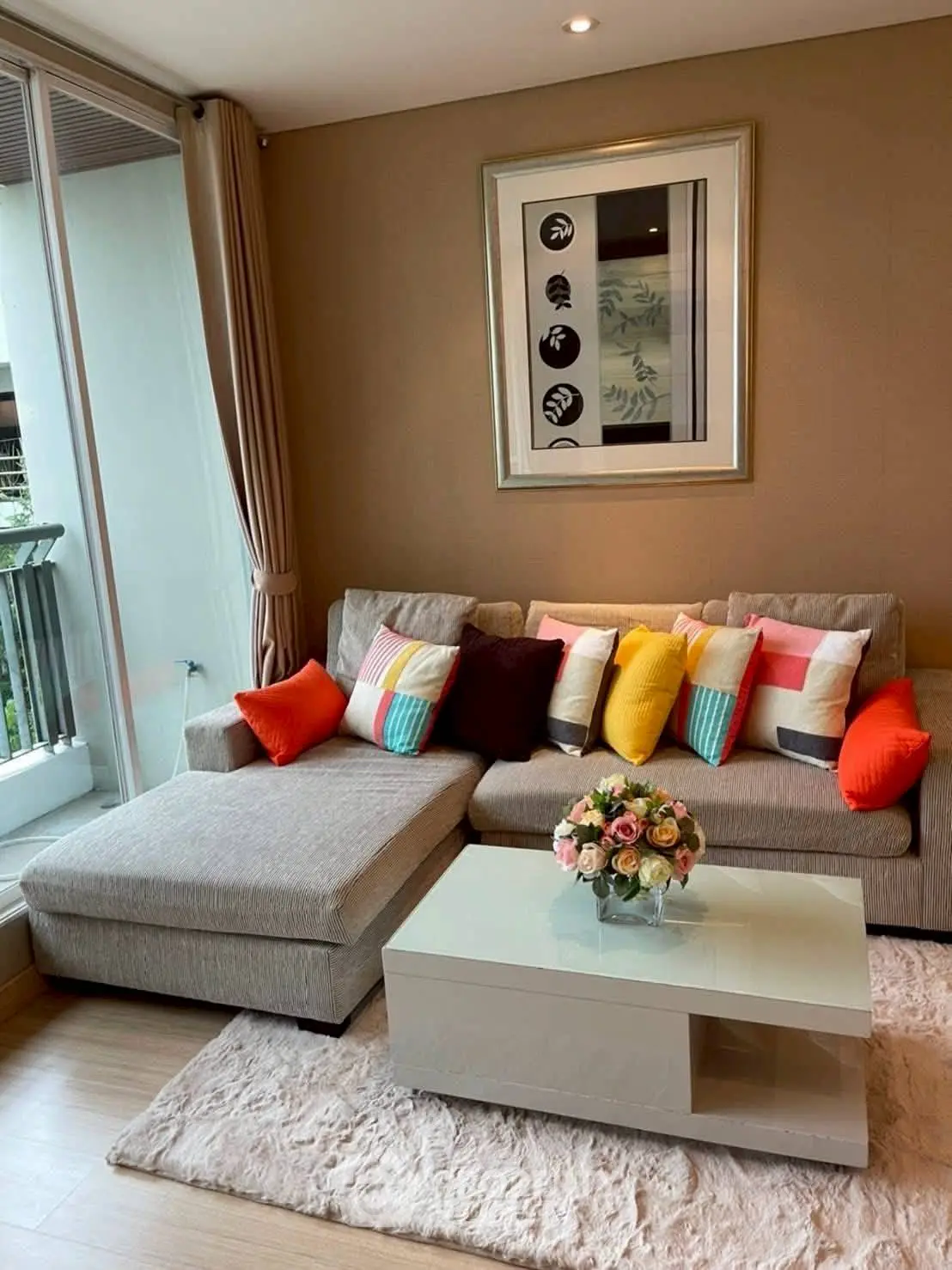 Stylish living room with modern sofa and colorful cushions, featuring a glass coffee table and balcony view.