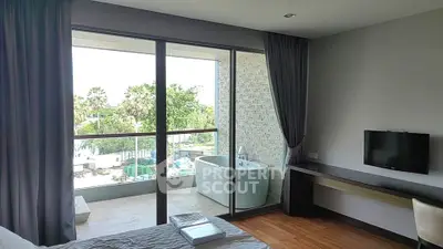 Modern bedroom with balcony and outdoor bathtub overlooking lush greenery.