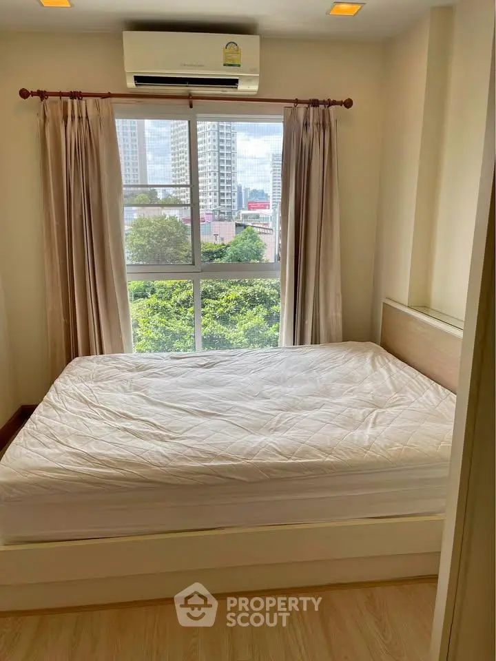 Cozy bedroom with large window offering city and greenery views, featuring a comfortable bed and air conditioning.