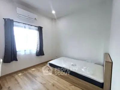 Minimalist bedroom with single bed, air conditioning, and wooden flooring, perfect for cozy living.
