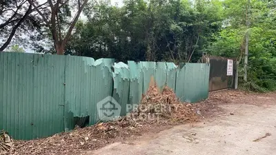 Damaged green fence with trees and foliage in a real estate setting