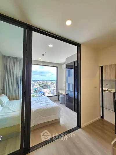 Modern bedroom with floor-to-ceiling windows offering stunning city views, adjacent to a sleek kitchen.