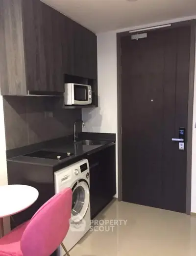 Modern compact kitchen with washing machine and microwave in sleek apartment.