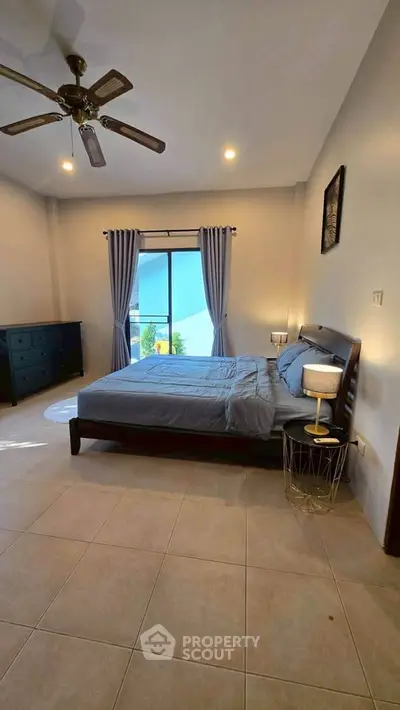 Spacious bedroom with modern decor and natural light, featuring a ceiling fan and stylish furnishings.