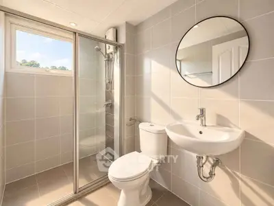 Modern bathroom with sleek design, featuring a round mirror, glass shower, and natural light.