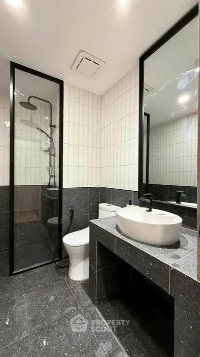 Modern bathroom with sleek black and white design, featuring a glass shower and stylish fixtures.