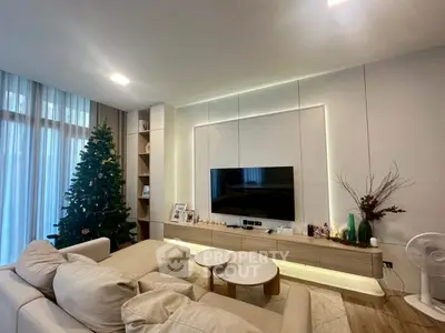 Modern living room with elegant decor and Christmas tree, featuring a large TV and cozy seating area.