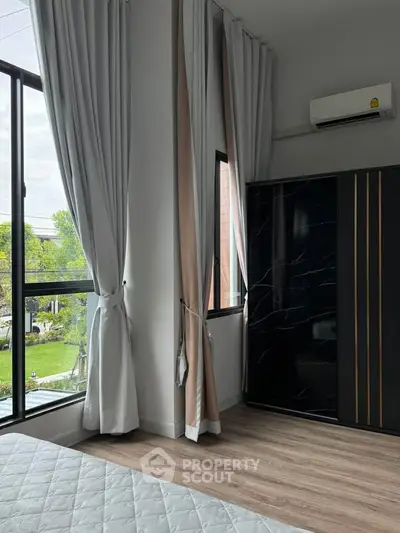 Modern bedroom with large windows and elegant curtains, featuring a sleek black wardrobe and air conditioning.