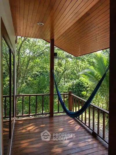 Charming wooden balcony with hammock overlooking lush greenery, perfect for relaxation and nature lovers.
