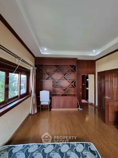 Spacious bedroom with wooden flooring and built-in shelving, large window for natural light.