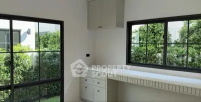 Bright study room with large windows and built-in desk overlooking lush garden.