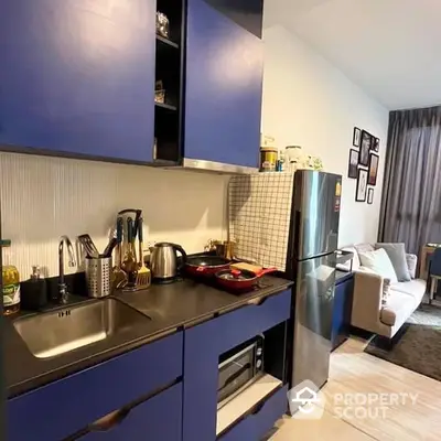 Modern kitchen with blue cabinets, stainless steel appliances, and an open layout leading to a cozy living area with elegant decor.