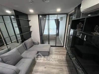 Modern living room with sleek design and mirrored wall, leading to a cozy bedroom through glass doors.