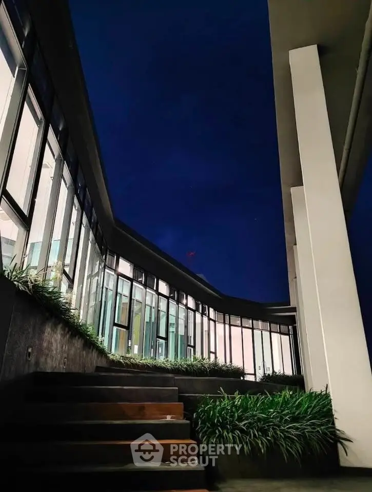 Stunning modern building exterior with sleek design and lush greenery at night.