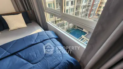 Cozy bedroom with city view and modern furnishings, overlooking a pool area.