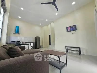 Modern living room with open kitchen, sleek furniture, and ceiling fan in a spacious interior.