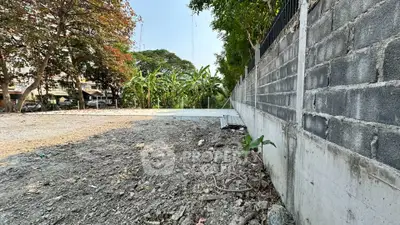 Vacant land plot with potential for development, surrounded by lush greenery and a sturdy boundary wall.