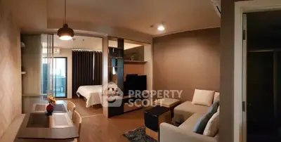 Modern open-plan living room with cozy seating and stylish decor, leading to a bedroom with natural light.